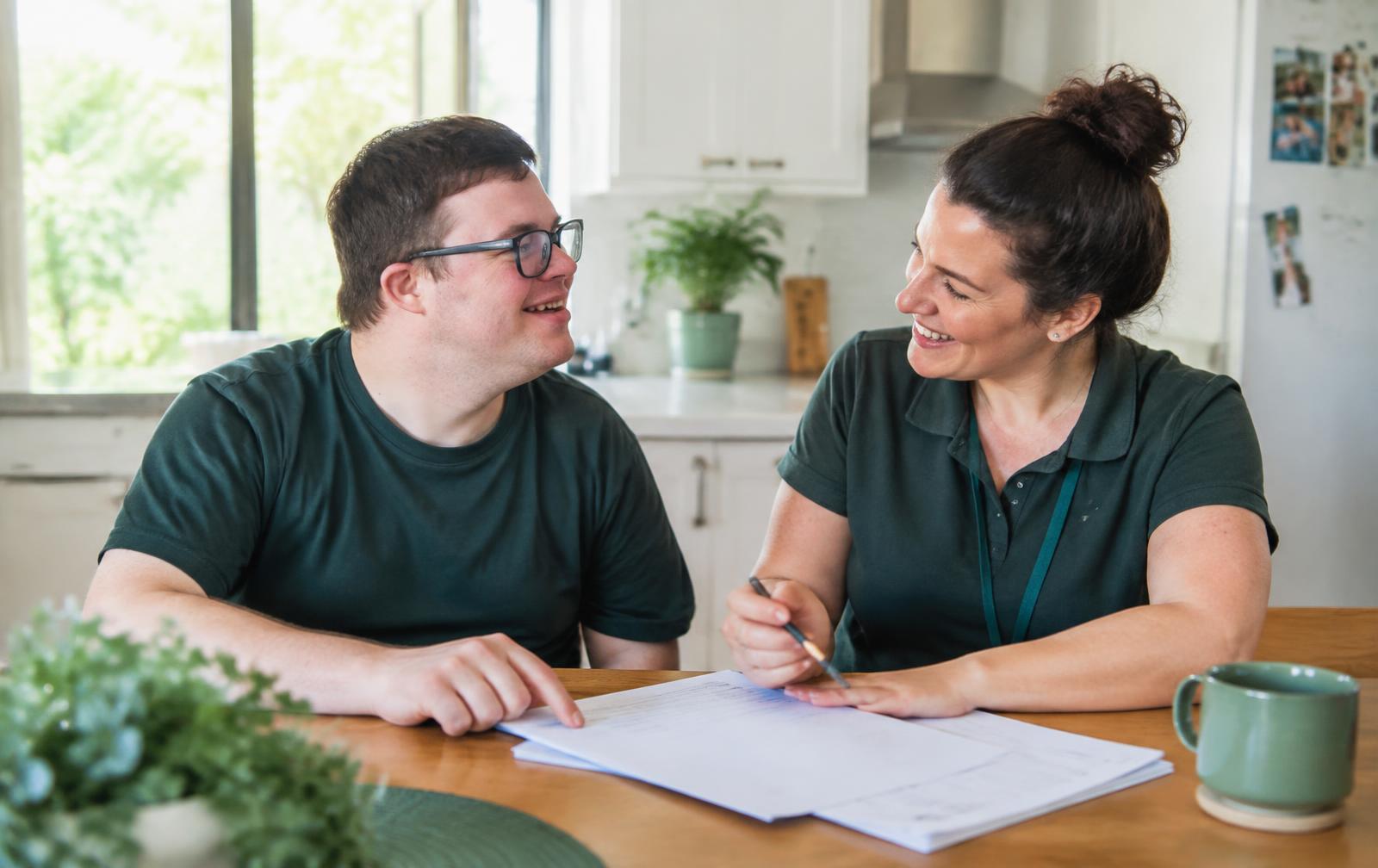 A support worker and a participant reviewing plan paperwork at a kitchen table